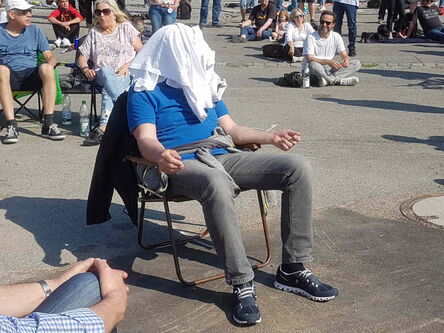 Mann im blauen Shirt im Klappstuhl mit weißem Shirt als Kopfbedeckung