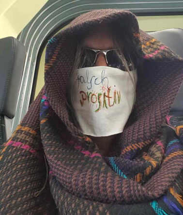 Person in gemustertes Tuch gehüllt mit weißem Leinen um Mund und Nase und Sonnenbrille