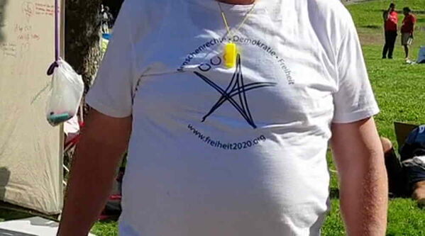 Mann im weißen Shirt mit schwarzem Pentagramm und gelber flöte um den Hals