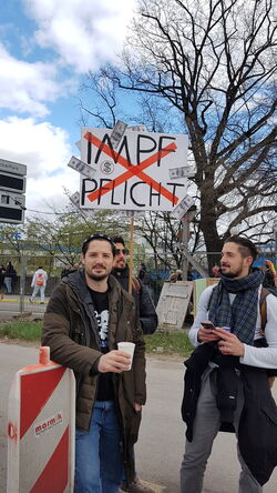 Drei Männer ein Plakat auf dem "Geldscheine" und das durchgestrichene Wort „Impfpflich" zu sehen sind.