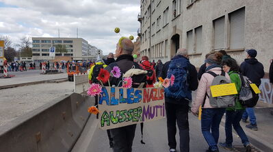 Ein Herr als Bienchen geschmückt mit Blümchen um das bunte Plakat