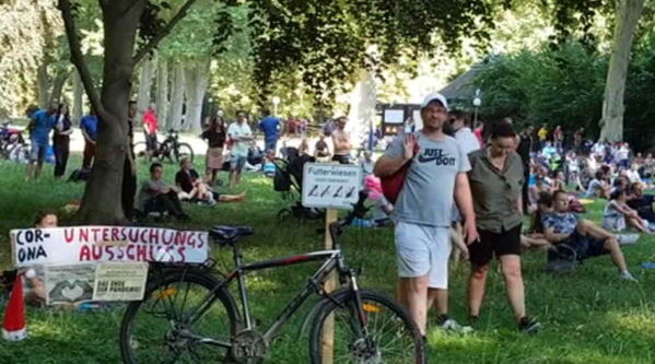 Schattige Plätze für Demobesucher in Liegestühlen unter Bäumen. Hinweisschild schwarz und rot auf weißem Hintergrund