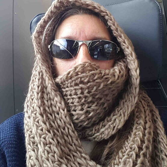 Person mit Sonnenbrille von grobmaschigem Schal umhüllt.