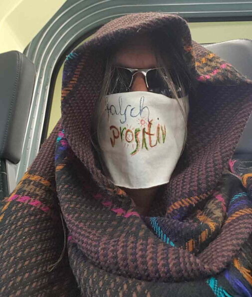 Person in gemustertes Tuch gehüllt mit weißem Leinen um Mund und Nase und Sonnenbrille