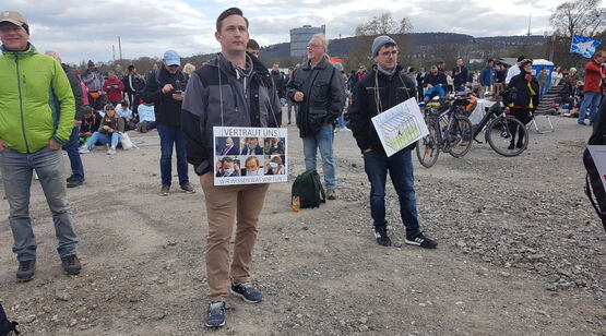 Links Mann mit Plakat: Fotos von Politikern. - Rechts Mann mit Plakat-Zeichnung: Vogel im Käfig