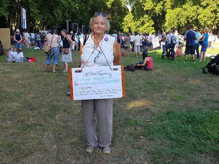 Frau mit vertikal blau weiß gestreifter Hose und weißen Hemd, mit großem Schild um den Hals