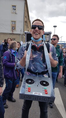 Junger Mann, DJ mit Sonnenbrille, Kopfhörern und Mischpult-Atrappe um den Hals