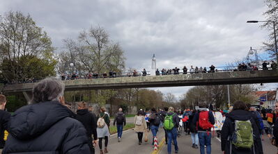 „Menschenmenge bei Demo, die unter einer Fußgängerbrücke hindurchläuft, Zuschauer auf der Brücke.“