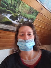 Maske unter der Nase getragen vor einem Naturposter im Wald