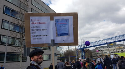 Mann mit Plakat-Tafel mit Hinweis auf Testzentren