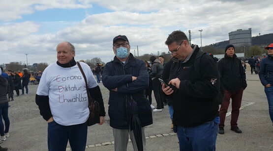 Drei Domonstranten: Einer im weißen Shirt, einer mit Maske, einer ließst am Phone