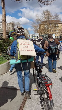 Fahradfahrerin mit Plakat auf dem Rücken.