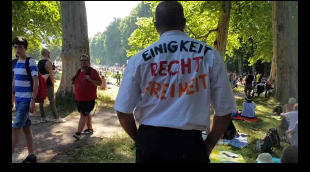 Ein Mann im T-Shirt. Die Rückseite bedruckt: Schwarz „Einigkeit", Rot „Recht", Gelb „Freiheit".